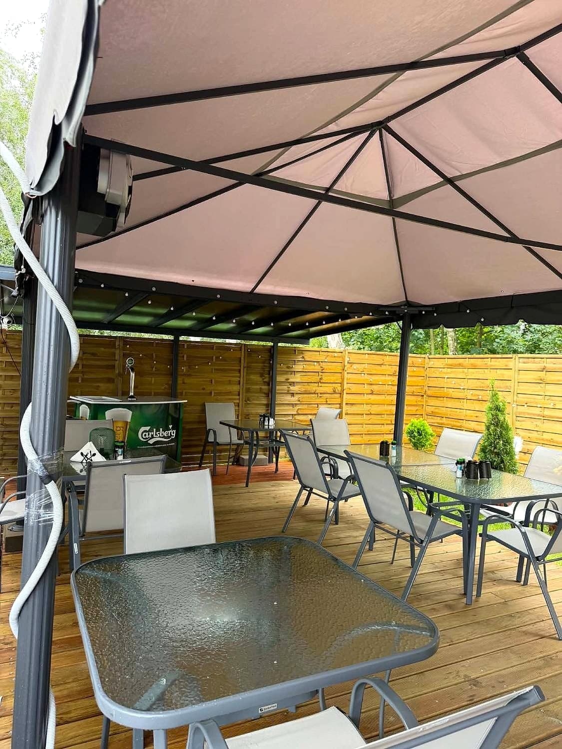 Ogródek restauracji pod zadaszeniem z drewnianym tarasem i szklanymi stolikami