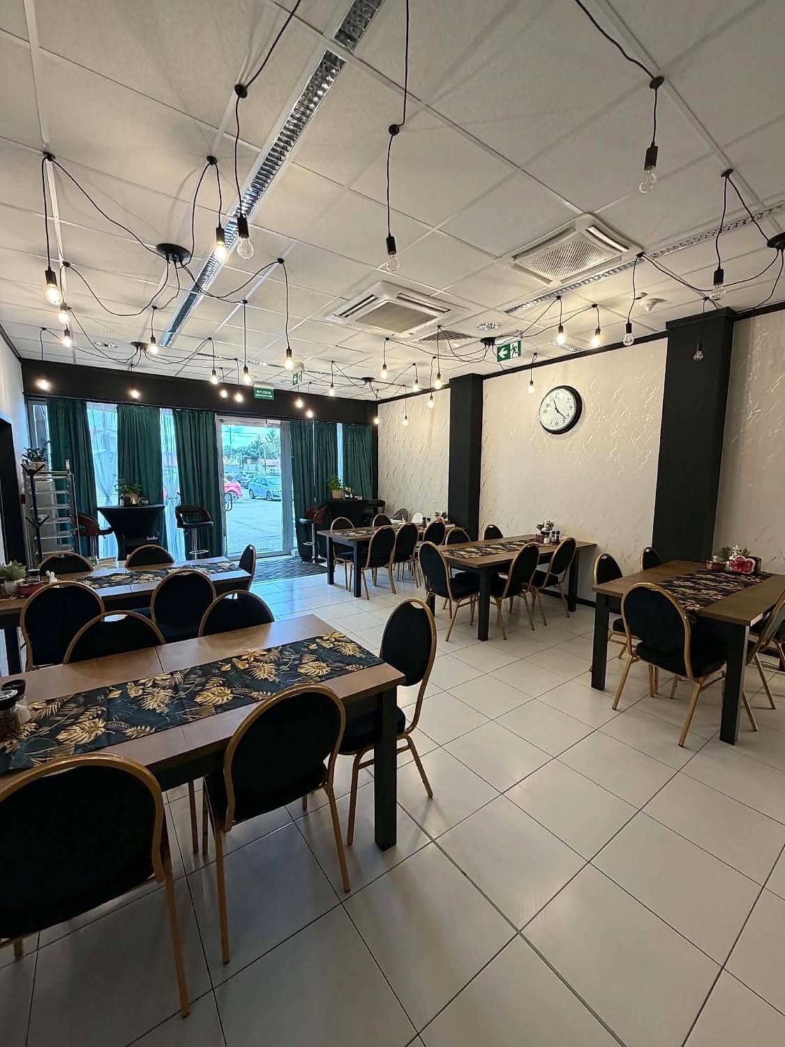 Sala restauracji z drewnianymi stołami, czarnymi krzesłami i wiszącymi żarówkami